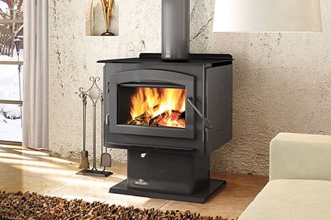 Stock photo of freestanding wood stove-Black Velvet Chimney Napoleon wood burning stove with roaring fire tools to the left leather rug on the floor